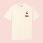 An off-white short-sleeve crewneck t-shirt with a small dark red graphic on the left chest depicting a sailboat and the text 'A VERY CHERRY SUMMER!', displayed against a solid pale pink background.
